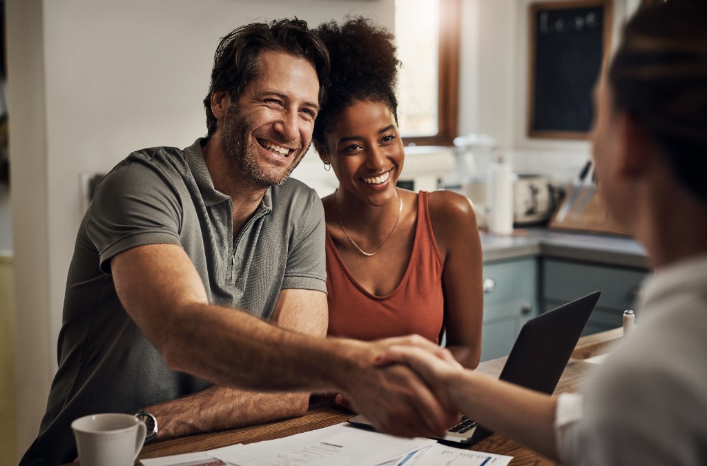 A smiling couple shaking hands with an advisor over planning documents